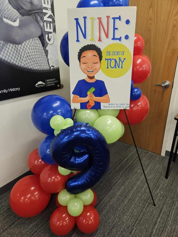 The book displayed at a launch event with festive balloons spelling out '9'